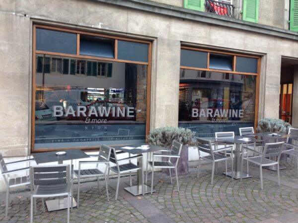 Vitrines du bar BARAWINE à Nyon avec lettrage adhésif blanc et terrasse extérieure équipée de tables et chaises métalliques