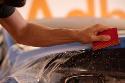 Nettoyage d'une voiture avec une éponge rouge.