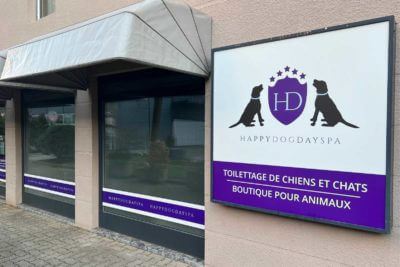 Enseigne extérieure du salon HappyDogDaySpa avec logo violet HD, silhouettes de chien et chat, et vitrine décorée pour toilettage et boutique animaux