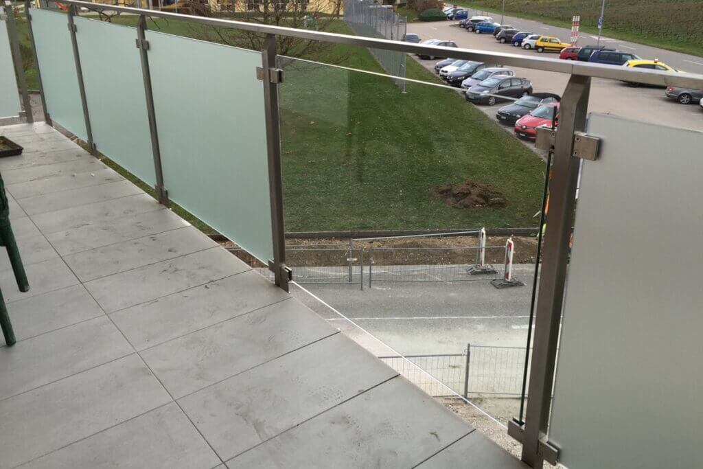 Balcon avec rambarde en verre et vue sur parking.