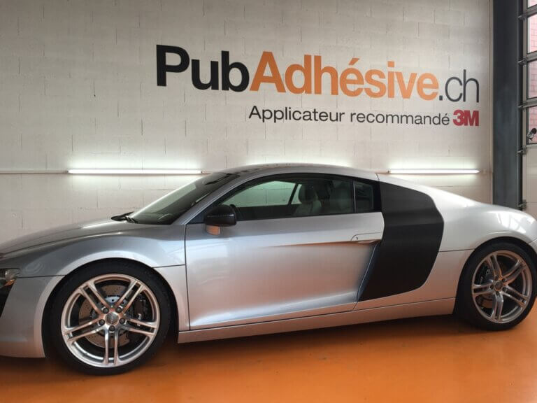 Voiture grise garée dans un atelier avec publicité.