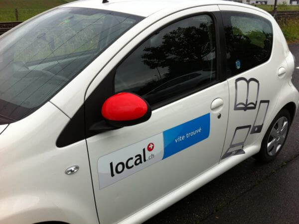 Voiture avec publicité local.ch et rétro rouge.