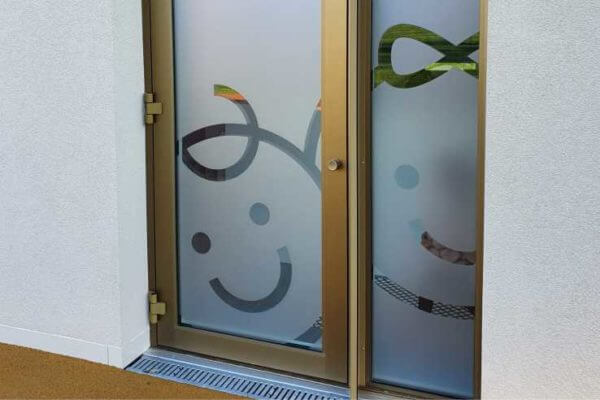Porte vitrée avec visages souriants dessinés.