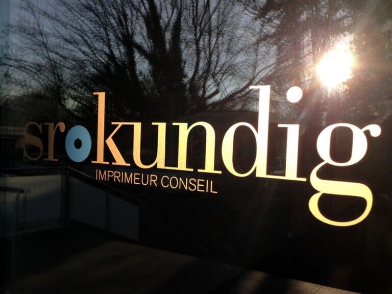 Inscription Sro Kundig sur vitre, fond arboré.