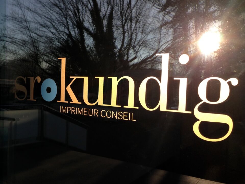 Inscription Sro Kundig sur vitre, fond arboré.